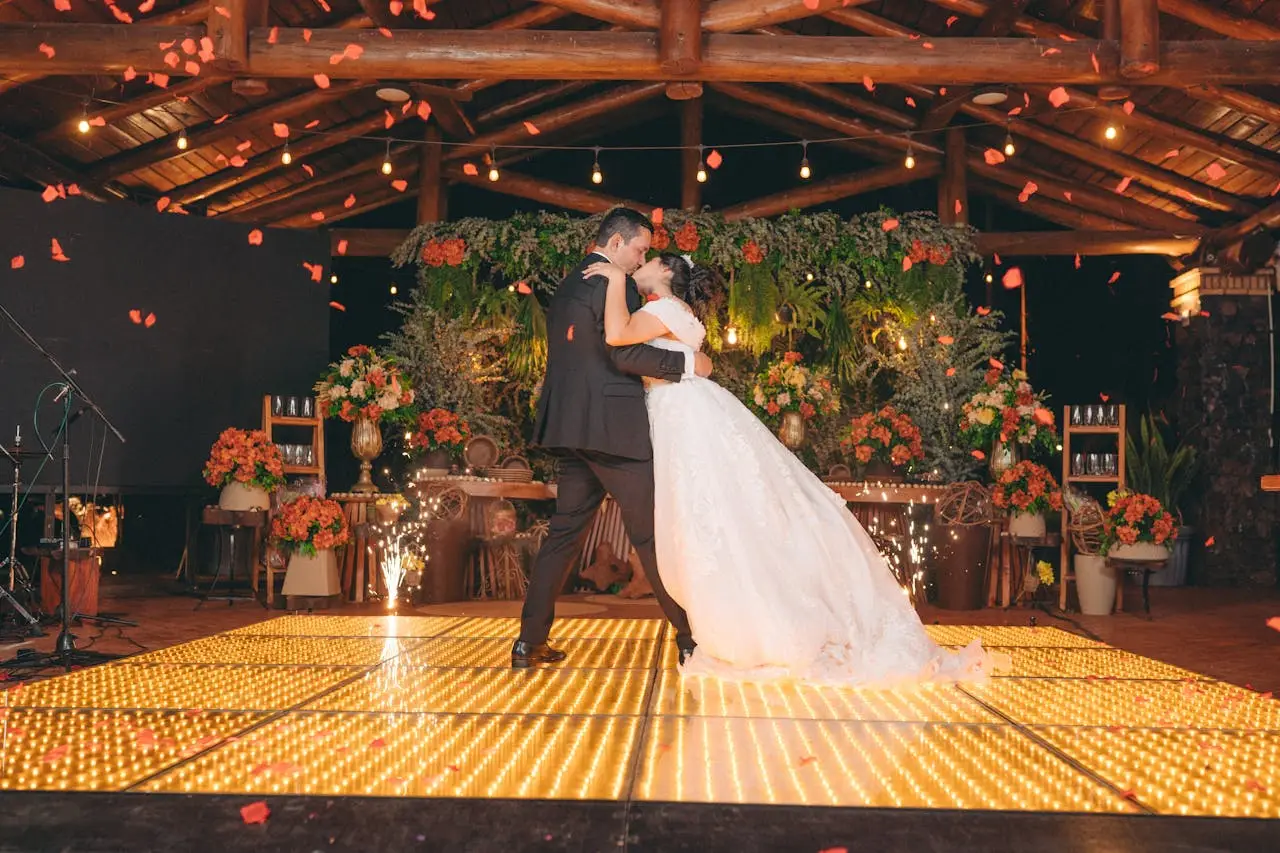 Bride and groom share a romantic first dance on a floral-decorated, illuminated dance floor.
